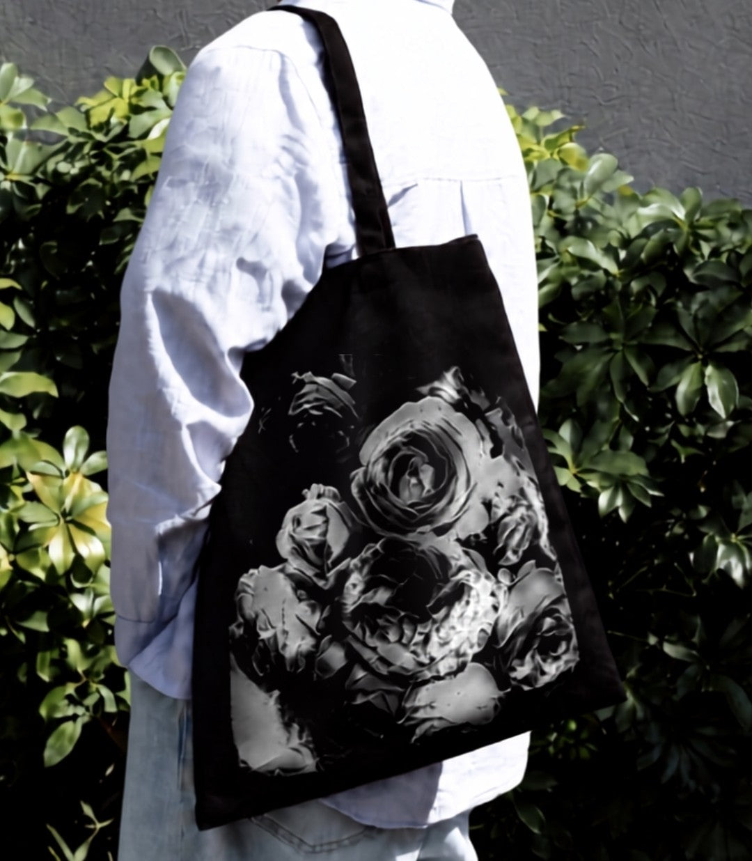 Black tote bag with long handles and a black-and-white floral print, worn over the shoulder outdoors.